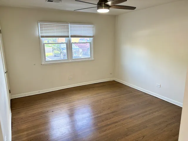 an empty room with wooden floor fan and windows