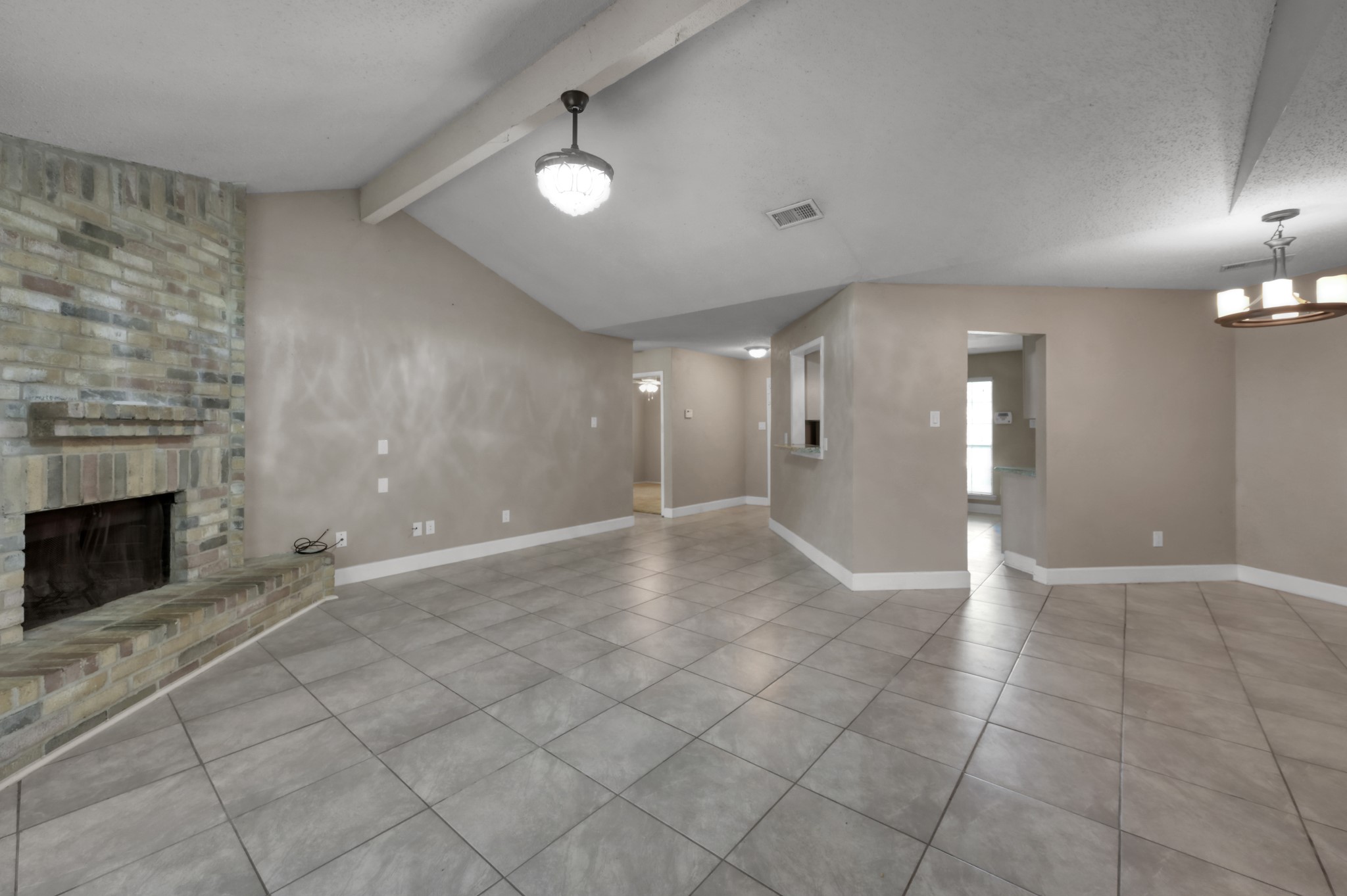 12015 Fallbrook Drive Houston, TX 77065 - Photo 7 of 29 This spacious living area features a high ceiling, tiled flooring, and a brick fireplace. It has neutral-colored walls and modern lighting, providing an inviting and versatile space for relaxation or gatherings.