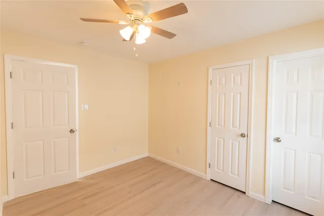 an empty room with wooden floor closet fan and windows
