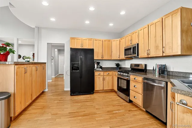 a kitchen with stainless steel appliances granite countertop a refrigerator a stove top oven a sink and dishwasher with wooden floor