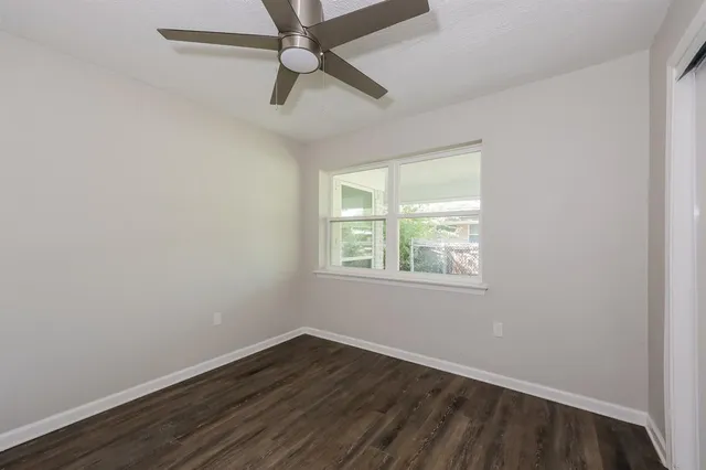 an empty room with wooden floor fan and windows