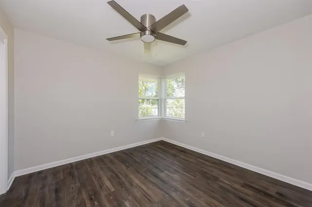 an empty room with wooden floor ceiling fan and windows