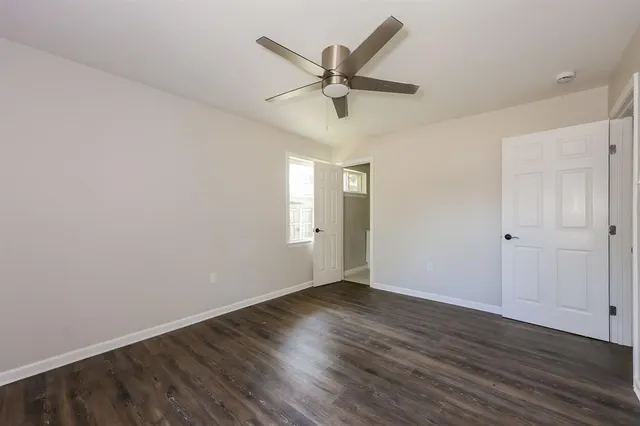 a view of an empty room with wooden floor and a ceiling fan