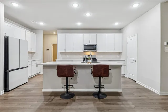 a kitchen with a refrigerator a stove a sink and white cabinets with wooden floor