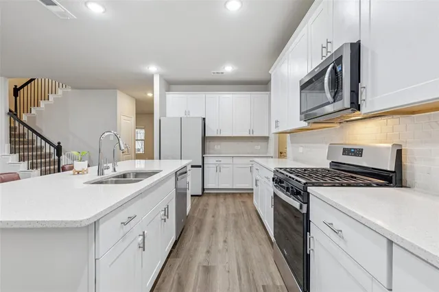 a kitchen with stainless steel appliances granite countertop a sink stove oven and white cabinets with wooden floor