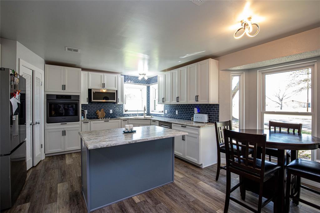 735 Willow Grove Road Woodway, TX 76712 - Photo 7 of 39 a kitchen with stainless steel appliances granite countertop a stove a refrigerator a sink dishwasher a dining table and chairs with wooden floor