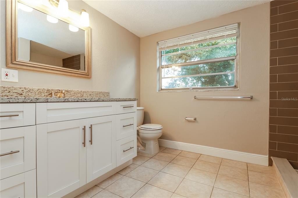 9226 Rainbow Lane Port Richey, FL 34668 - Photo 10 of 16 a bathroom with a granite countertop toilet a sink and a mirror