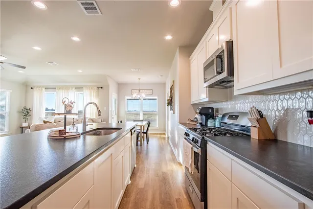 a kitchen with stainless steel appliances granite countertop a stove top oven a sink dishwasher a dining table and chairs with wooden floor