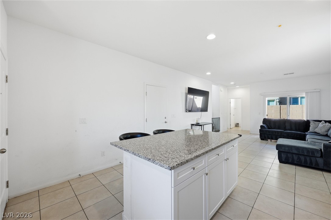 1811 Lincoln Road Las Vegas, NV 89115 - Photo 28 of 30 Kitchen featuring a kitchen island, light stone counters, white cabinets, open floor plan, and a breakfast bar