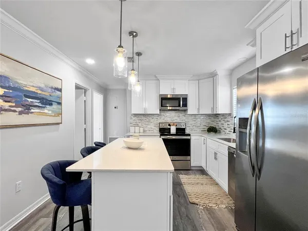 a kitchen with stainless steel appliances kitchen island granite countertop a refrigerator a sink dishwasher a stove with white cabinets and wooden floor