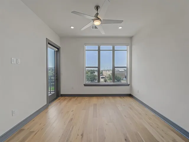 an empty room with wooden floor chandelier fan and windows