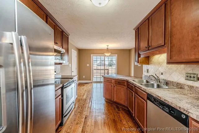 a kitchen with stainless steel appliances granite countertop a refrigerator a sink dishwasher a stove with wooden cabinets and floor