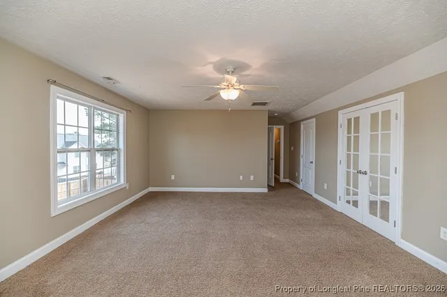 an empty room with chandelier fan and windows