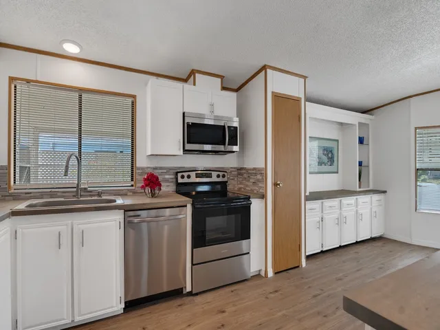 a kitchen with stainless steel appliances granite countertop a stove top oven a sink a refrigerator white cabinets and wooden floor