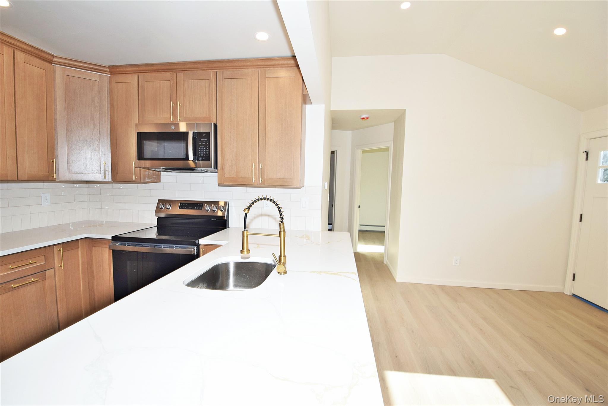 371 Oceanside Street Islip Terrace, NY 11752 - Photo 13 of 38 Kitchen with electric range, decorative backsplash, stainless steel microwave, vaulted ceiling, and light stone countertops
