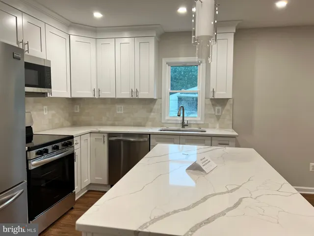 a kitchen with stainless steel appliances kitchen island granite countertop a stove a refrigerator a sink a dining table and chairs with wooden floor