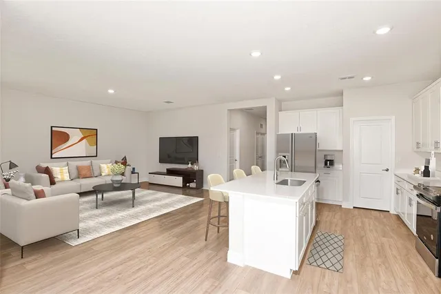 a living room with stainless steel appliances furniture a flat screen tv and a table