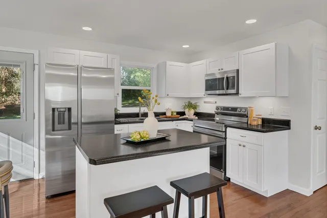 a kitchen with stainless steel appliances granite countertop a sink a stove a refrigerator cabinets and a dining table with wooden floor