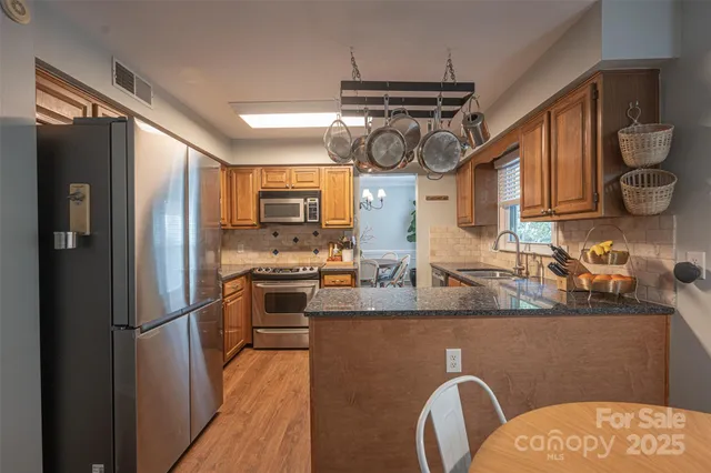 a kitchen with stainless steel appliances granite countertop a refrigerator a sink dishwasher a stove and a wooden cabinets