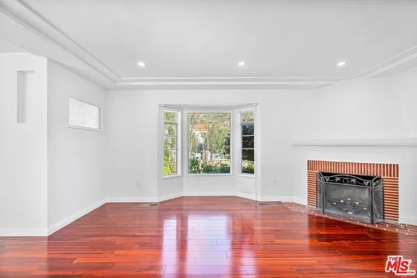 a view of an empty room with wooden floor fireplace and a window