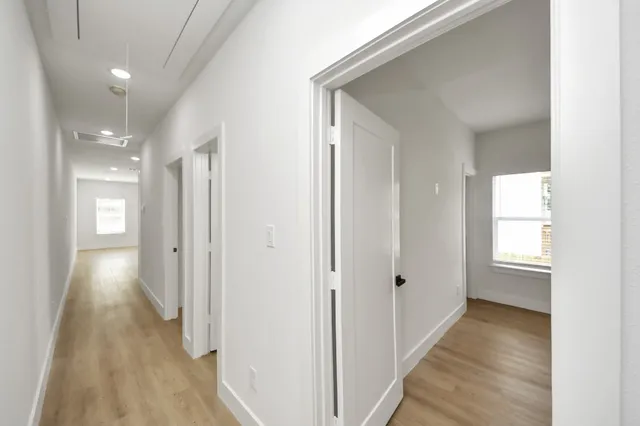 a view of a hallway with wooden floor and a bathroom