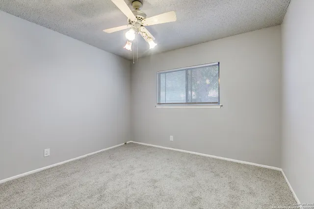 an empty room with a chandelier fan and windows