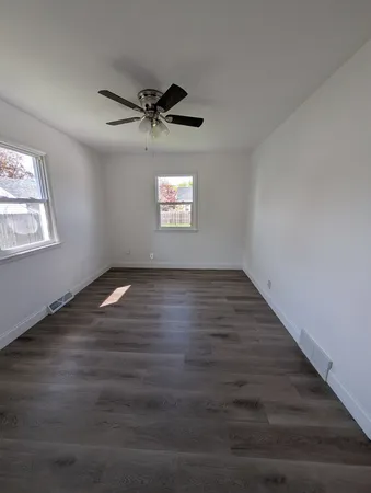 an empty room with wooden floor ceiling fan and windows