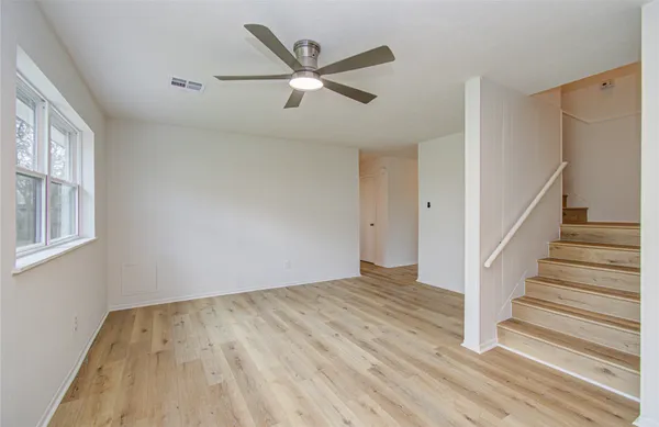 a view of an empty room with wooden floor and a ceiling fan