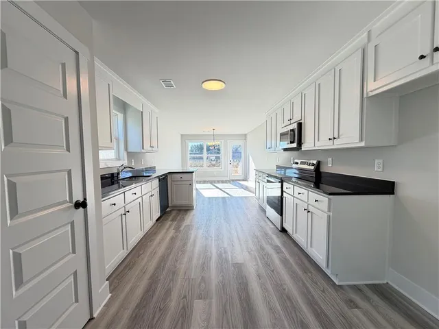 a kitchen with granite countertop a refrigerator oven a sink dishwasher and white cabinets with wooden floor