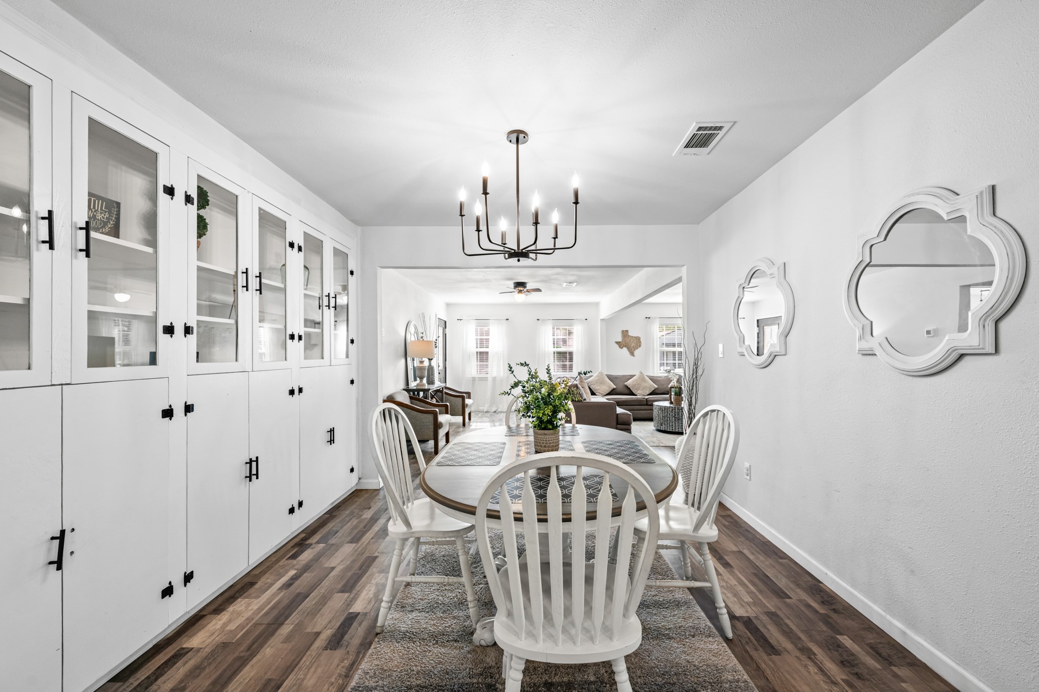 729 Kyle Angleton, TX 77515 - Photo 8 of 36 This photo showcases a bright dining area with built-in cabinets, a modern chandelier, and a round table with chairs. The space opens into a cozy living room, featuring wood-look flooring and decorative wall accents.