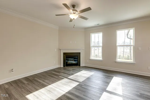 a view of an empty room with wooden floor fireplace and a window