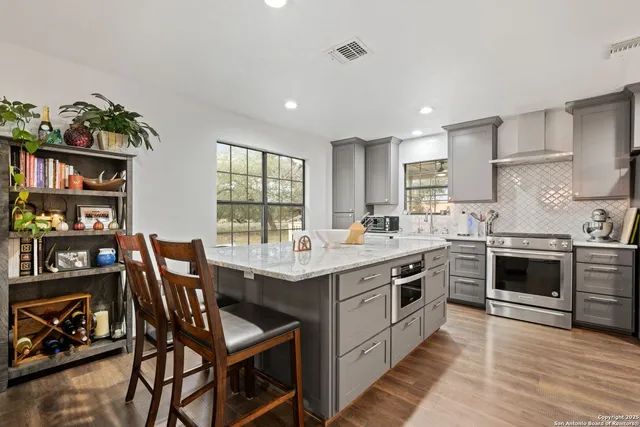 a kitchen with stainless steel appliances granite countertop a stove top oven a sink a dining table and chairs with wooden floor