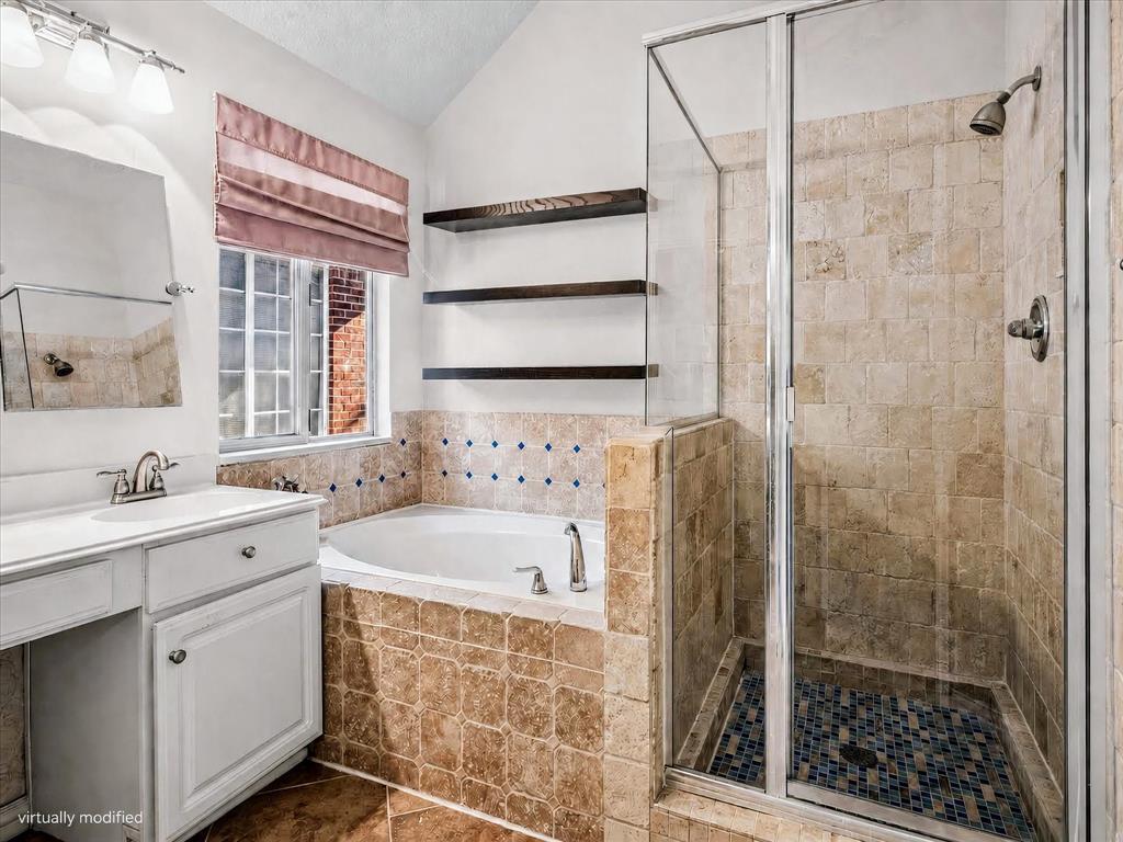14592 Greenleaf Court Addison, TX 75001 - Photo 19 of 34 Bathroom featuring a built-in tub with tile surround, a separate glass-enclosed shower with a mosaic tile floor, and a single vanity with storage cabinetry