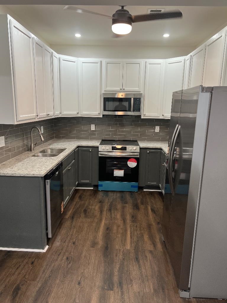 56 South Sanga Road Cordova, TN 38018 - Photo 11 of 26 Two tone kitchen featuring dual tone cabinetry, stainless steel appliances, light stone counters, tasteful backsplash, and dark wood-style floors