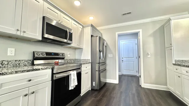 a kitchen with stainless steel appliances granite countertop white cabinets a sink a stove a microwave and wooden floors