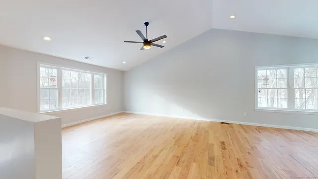 an empty room with wooden floor fan and windows