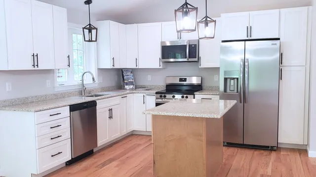 a kitchen with stainless steel appliances granite countertop a sink a stove a refrigerator and white cabinets with wooden floor