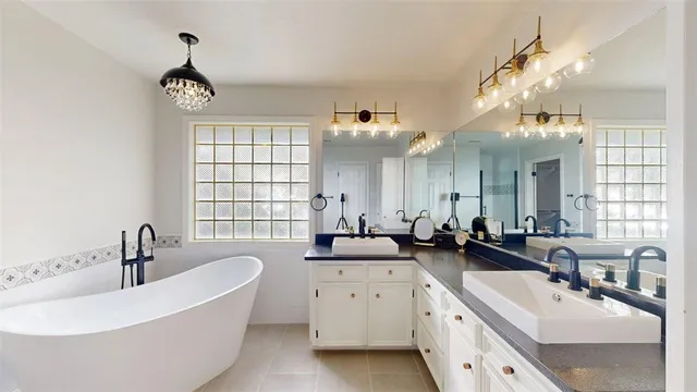 a bathroom with a tub a sink a large mirror and a bathtub next to a window