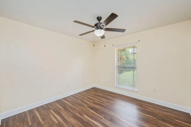 an empty room with wooden floor fan and windows