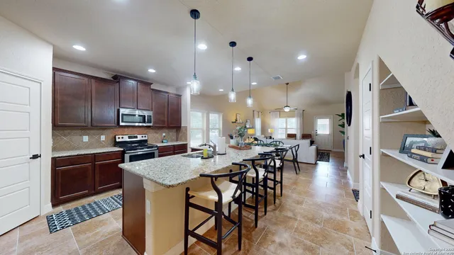 a kitchen with stainless steel appliances kitchen island granite countertop a refrigerator a stove a sink a dining table and chairs with wooden floor