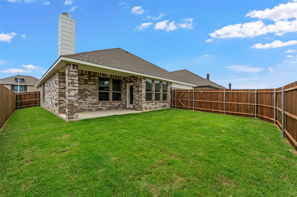 1508 Addison Lane Lancaster, TX 75134 - Photo 19 of 20 Expansive backyard featuring a manicured lawn, full perimeter privacy fencing, covered patio, and a multi-tone brick exterior with a prominent chimney structure
