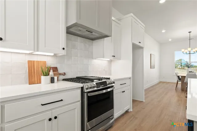 a kitchen with stainless steel appliances granite countertop a stove a sink and white cabinets
