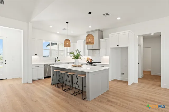 a kitchen with stainless steel appliances a stove top oven a sink dishwasher and a refrigerator with wooden floor