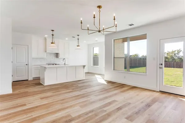 a view of an empty room and kitchen with wooden floor and windows