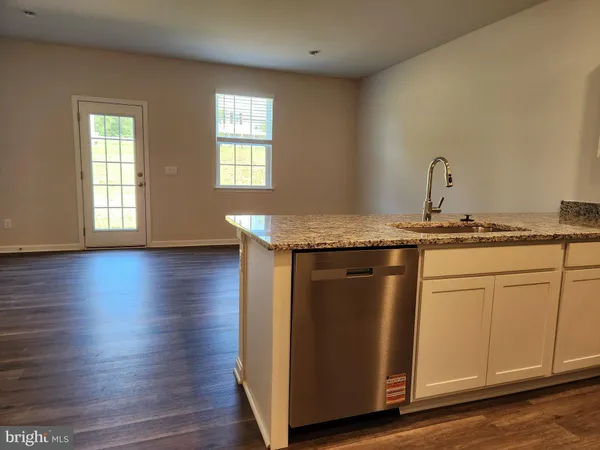 a room with kitchen island granite countertop wooden floors white cabinets and a sink