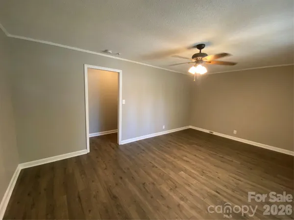 an empty room with wooden floor chandelier fan and windows