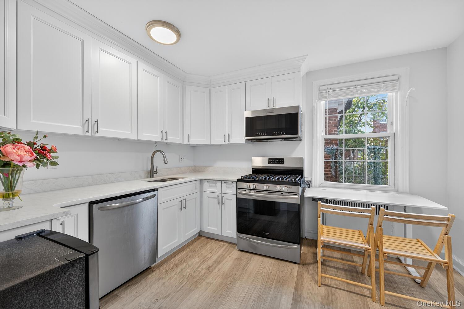 8 Welwyn Road, Unit 3F Great Neck, NY 11021 - Photo 6 of 17 Kitchen with appliances with stainless steel finishes, white cabinetry, light wood-style floors, and light stone countertops
