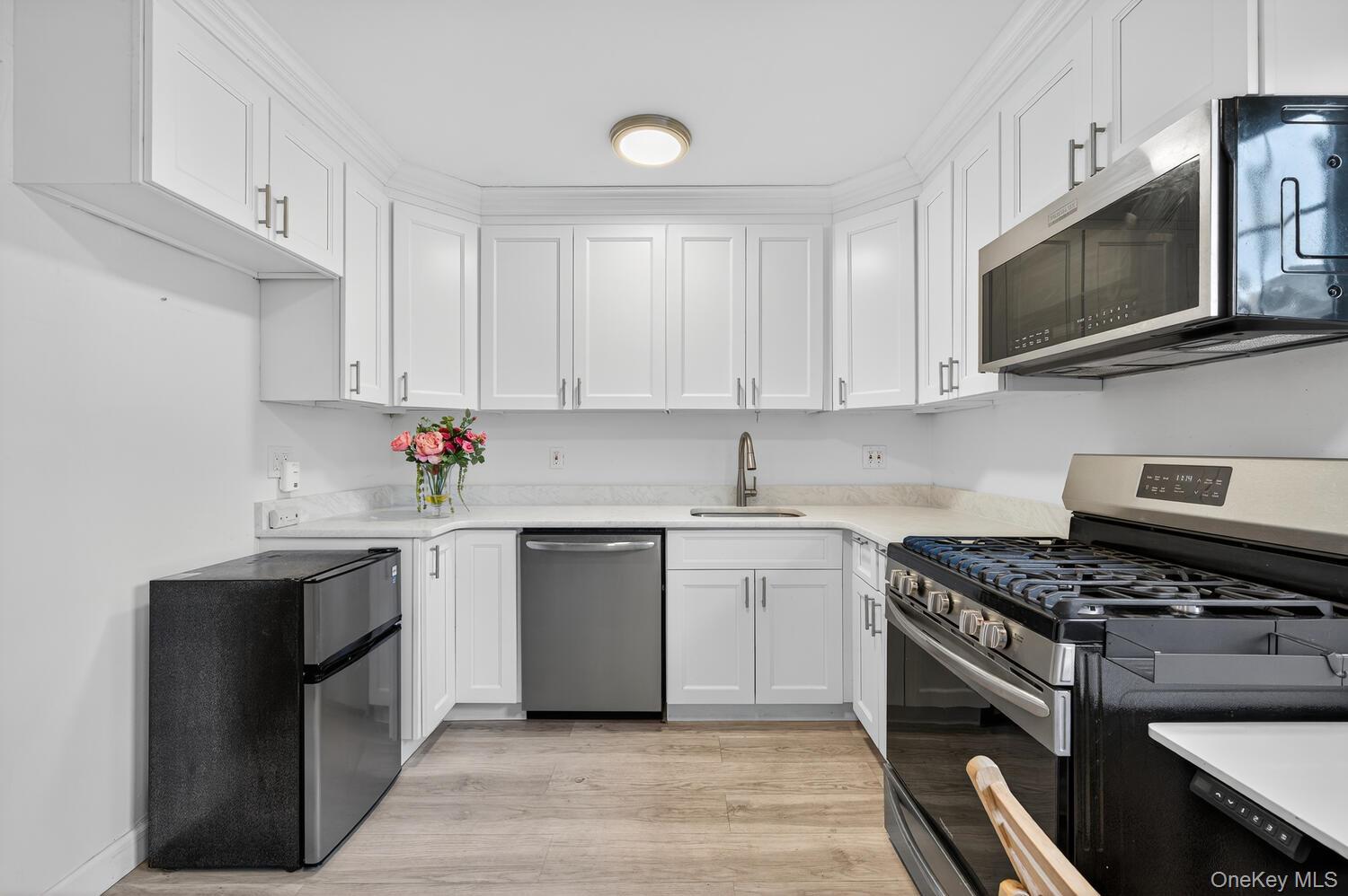 8 Welwyn Road, Unit 3F Great Neck, NY 11021 - Photo 7 of 17 Kitchen featuring stainless steel appliances, white cabinets, light wood-style flooring, and light stone countertops