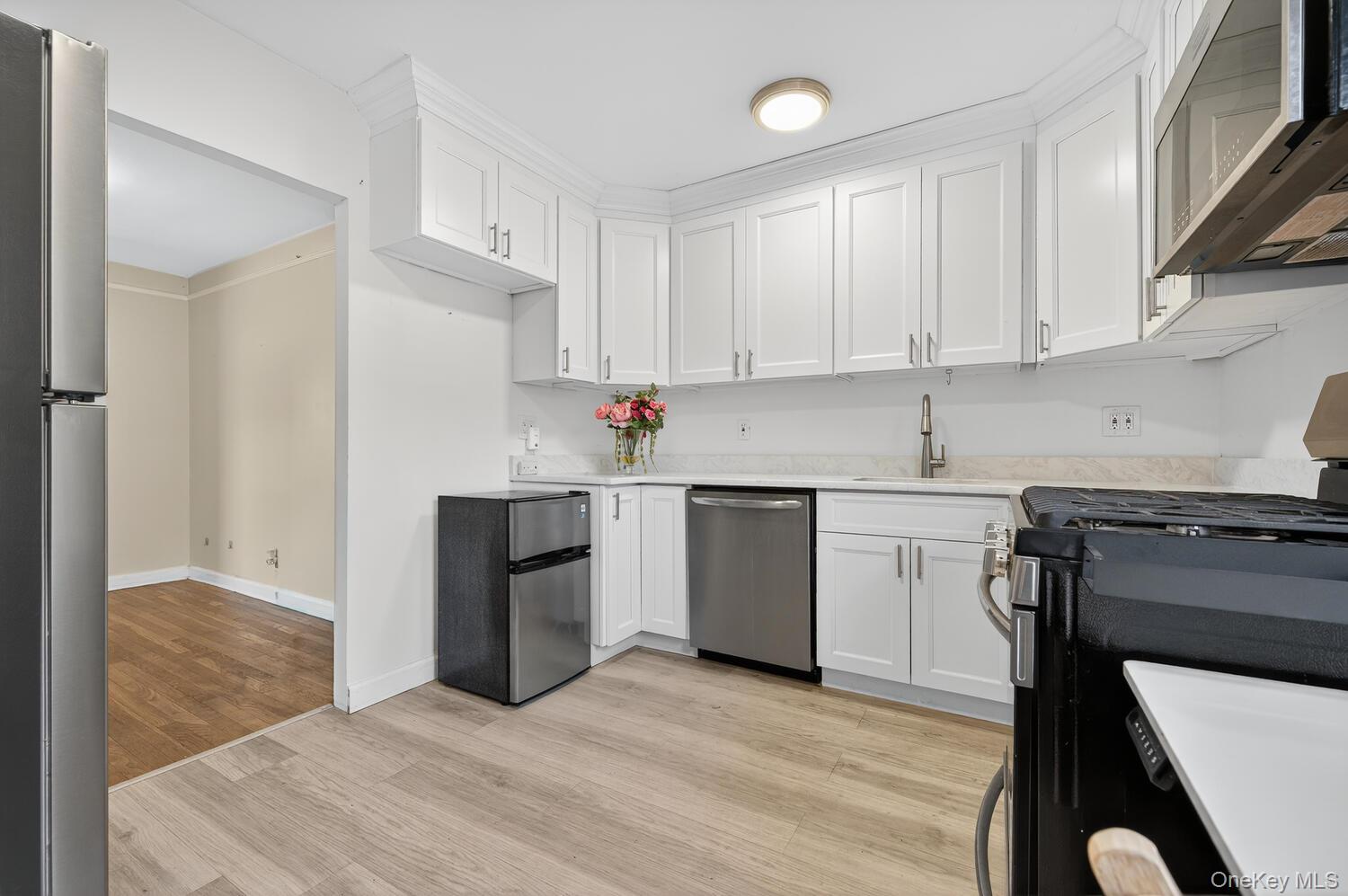 8 Welwyn Road, Unit 3F Great Neck, NY 11021 - Photo 8 of 17 Kitchen featuring appliances with stainless steel finishes, white cabinetry, light wood-style flooring, and light stone countertops