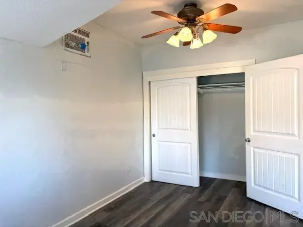 an empty room with a chandelier fan and wooden floor